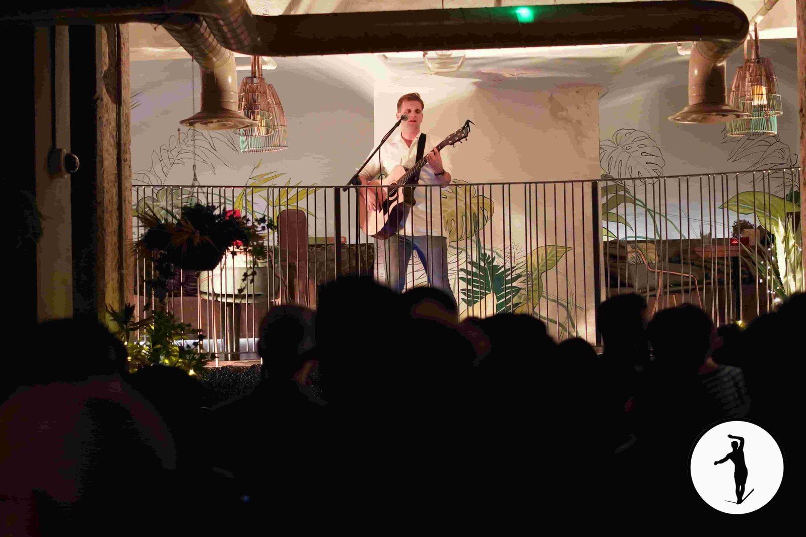 Musician with acoustic guitar performing on stage while guests watch at a Balancers night